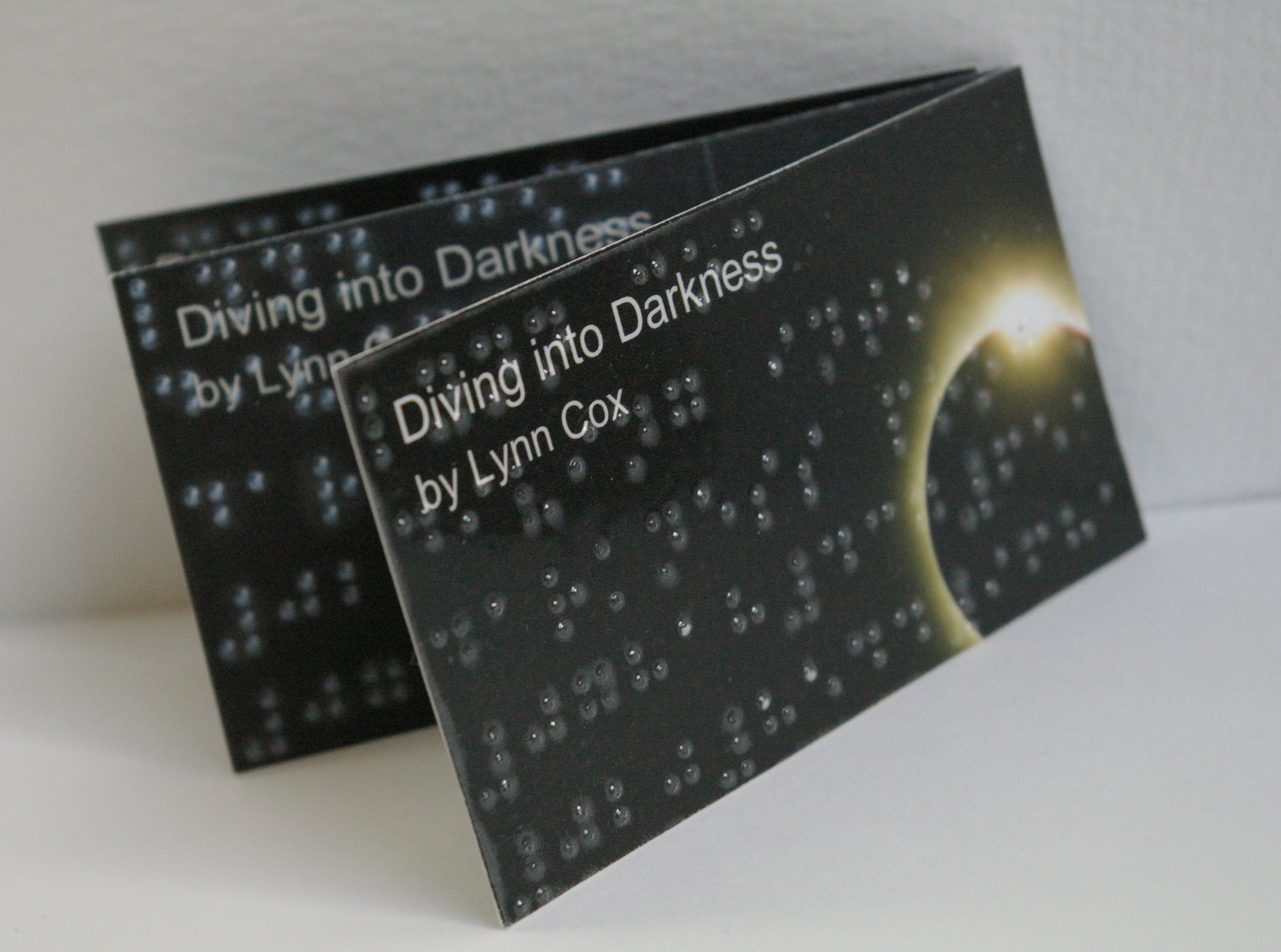 Three business cards landscape, arranged on a white background, in a fan type position showing Braille on each card. 